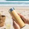 a person holding bamboo thermos by both the hands in the beach