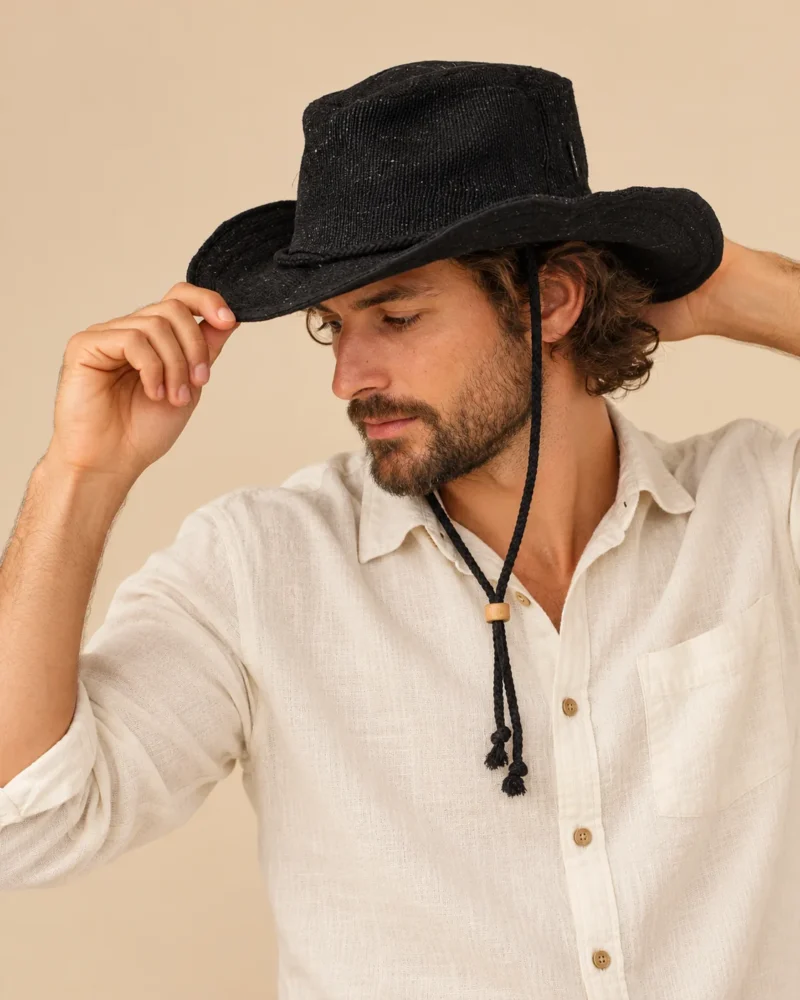Side view of male model wearing Black KTM Safari Hat with Chin String, holding the curved brim and showing the adjustable chin strap.
