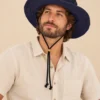 Male model wearing Navy Blue KTM Safari Hat with Chin String, featuring a wide shapable brim and adjustable black chin cord, styled with a natural hemp shirt.