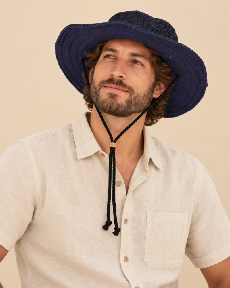 Male model wearing Navy Blue KTM Safari Hat with Chin String, featuring a wide shapable brim and adjustable black chin cord, styled with a natural hemp shirt.