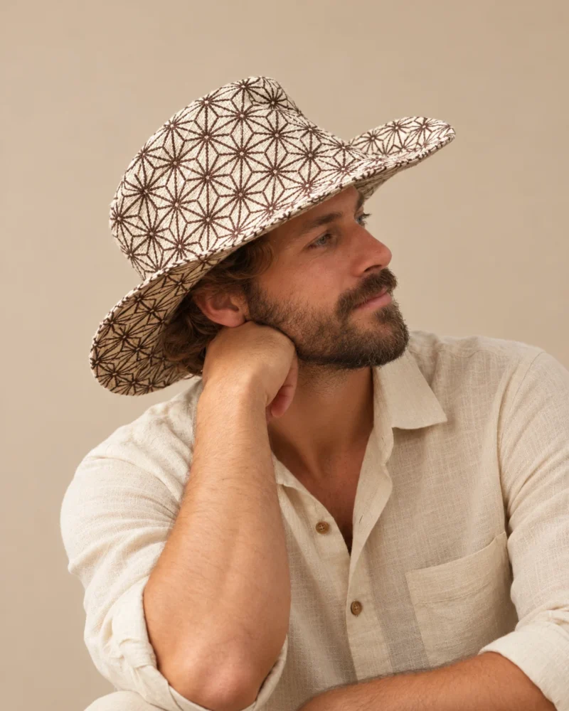 male model Maya wearing a beige wide-brim Himalayan hemp hat with brown cobweb print and natural linen shirt against a beige studio background.