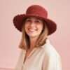 A woman wearing wide brim red crochet hat and smiling