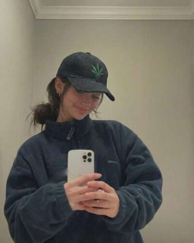 a woman wearing spreadmaya hemp leaf printed cap and taking a mirror selfie