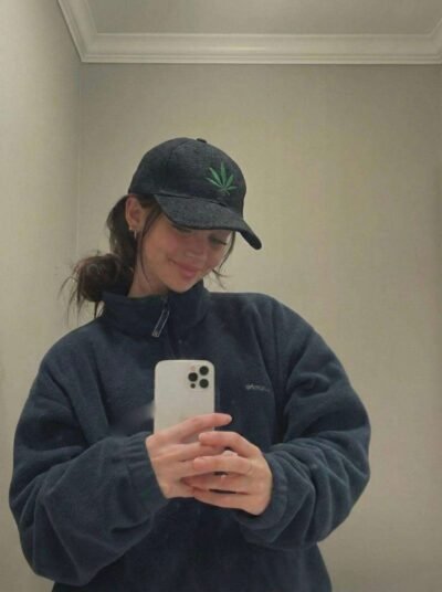 a woman wearing spreadmaya hemp leaf printed cap and taking a mirror selfie