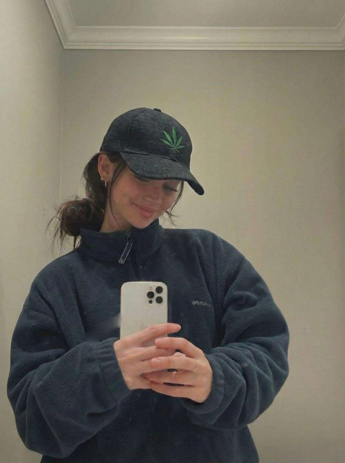 a woman wearing spreadmaya hemp leaf printed cap and taking a mirror selfie