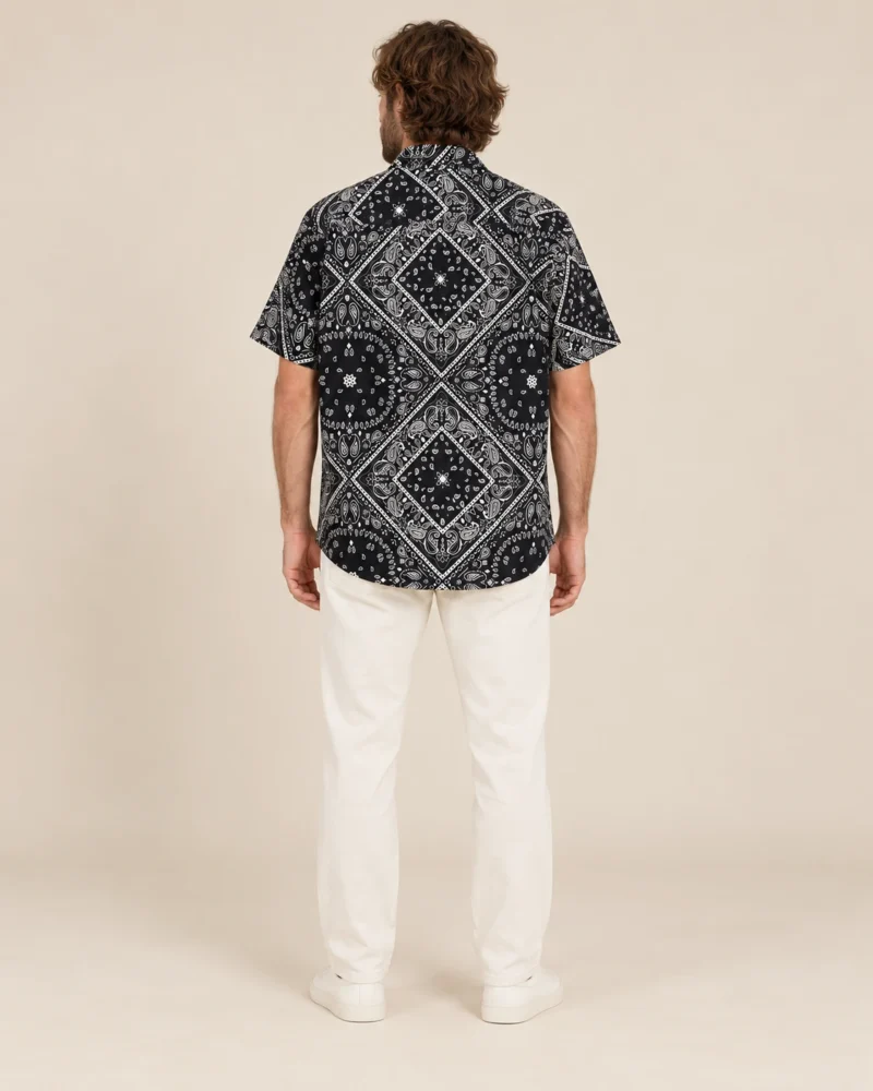 Back view of men’s black mandala hemp short sleeve shirt by Spreadmaya worn by male model on beige background.