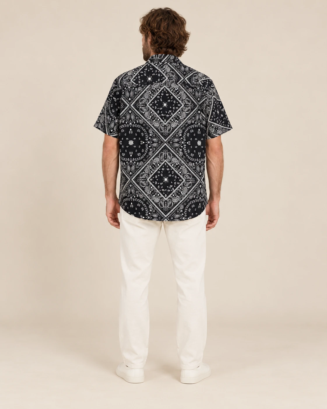 Back view of men’s black mandala hemp short sleeve shirt by Spreadmaya worn by male model on beige background.