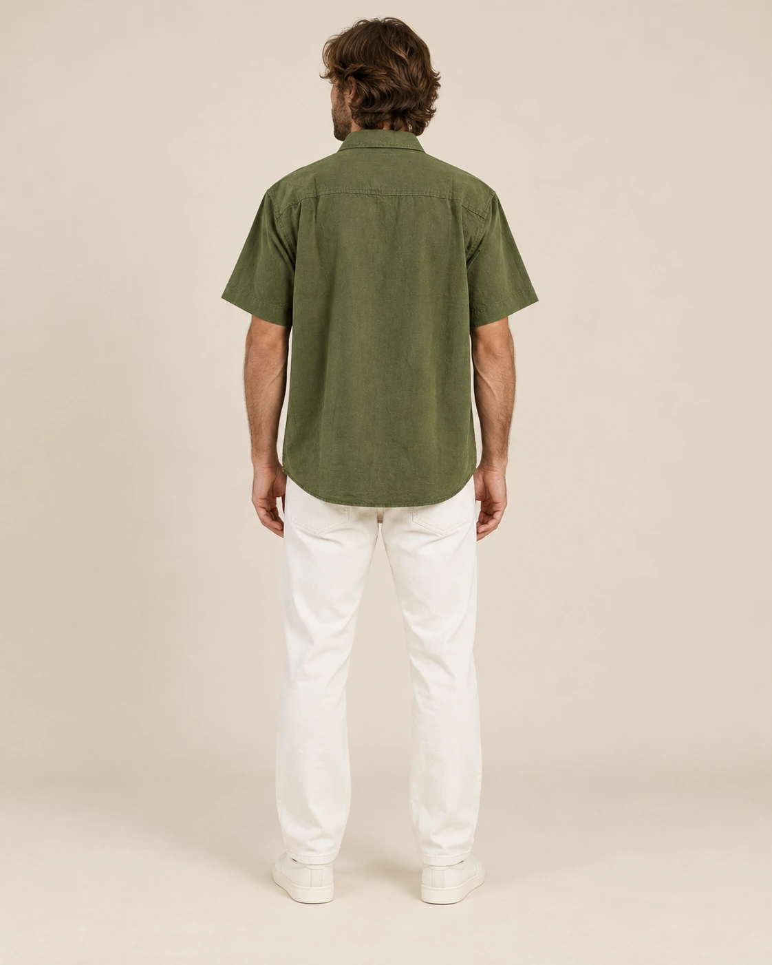 Back view of men’s olive green hemp short sleeve shirt by Spreadmaya worn by male model on beige background.